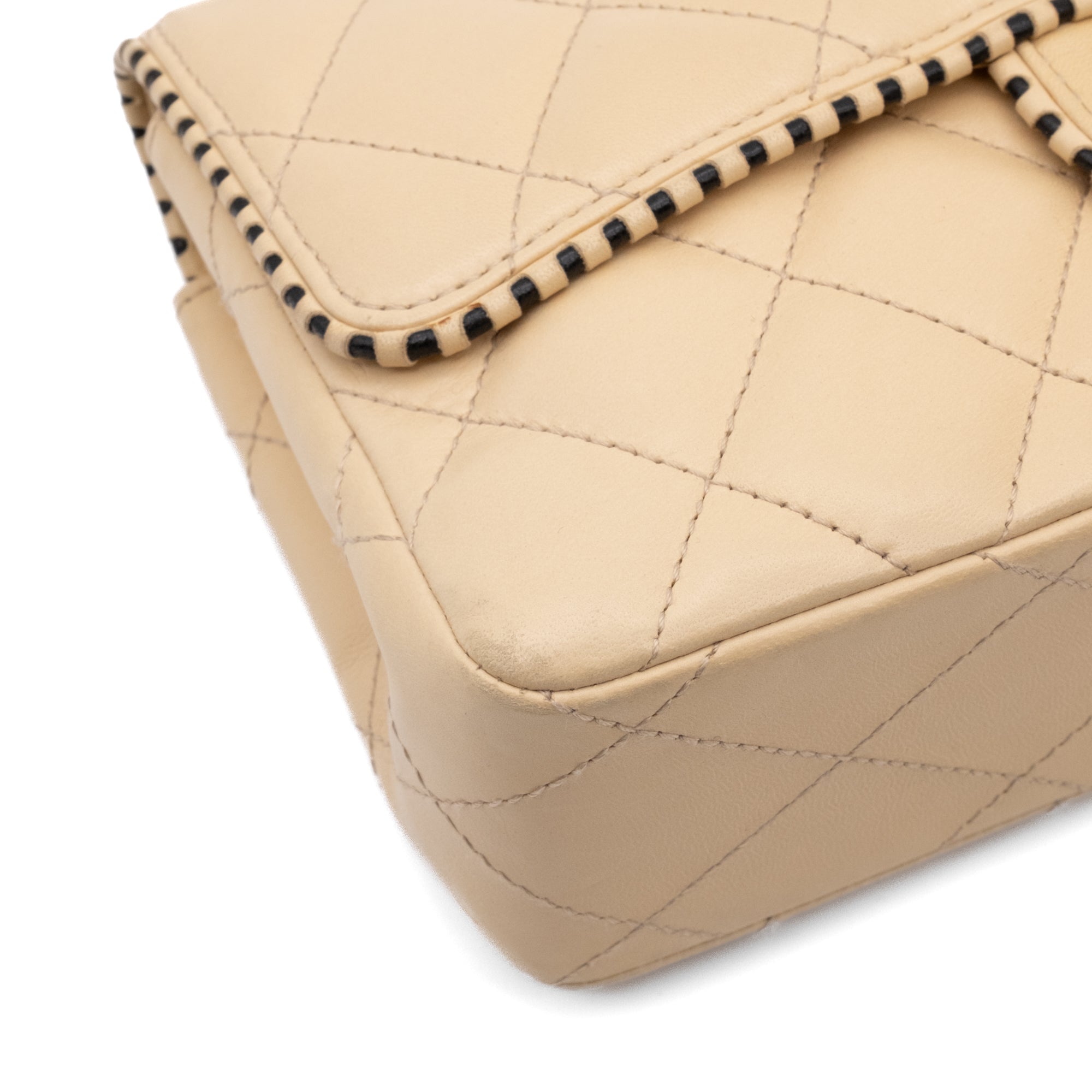 Beige Chanel Timeless Handtasche Single Flap Bag Medium Größe aus Lammleder Material mit goldener Hardware und schwarzer Trimm Zierborte Ecke vorne links
