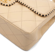 Beige Chanel Timeless Handtasche Single Flap Bag Medium Größe aus Lammleder Material mit goldener Hardware und schwarzer Trimm Zierborte Ecke vorne rechts 