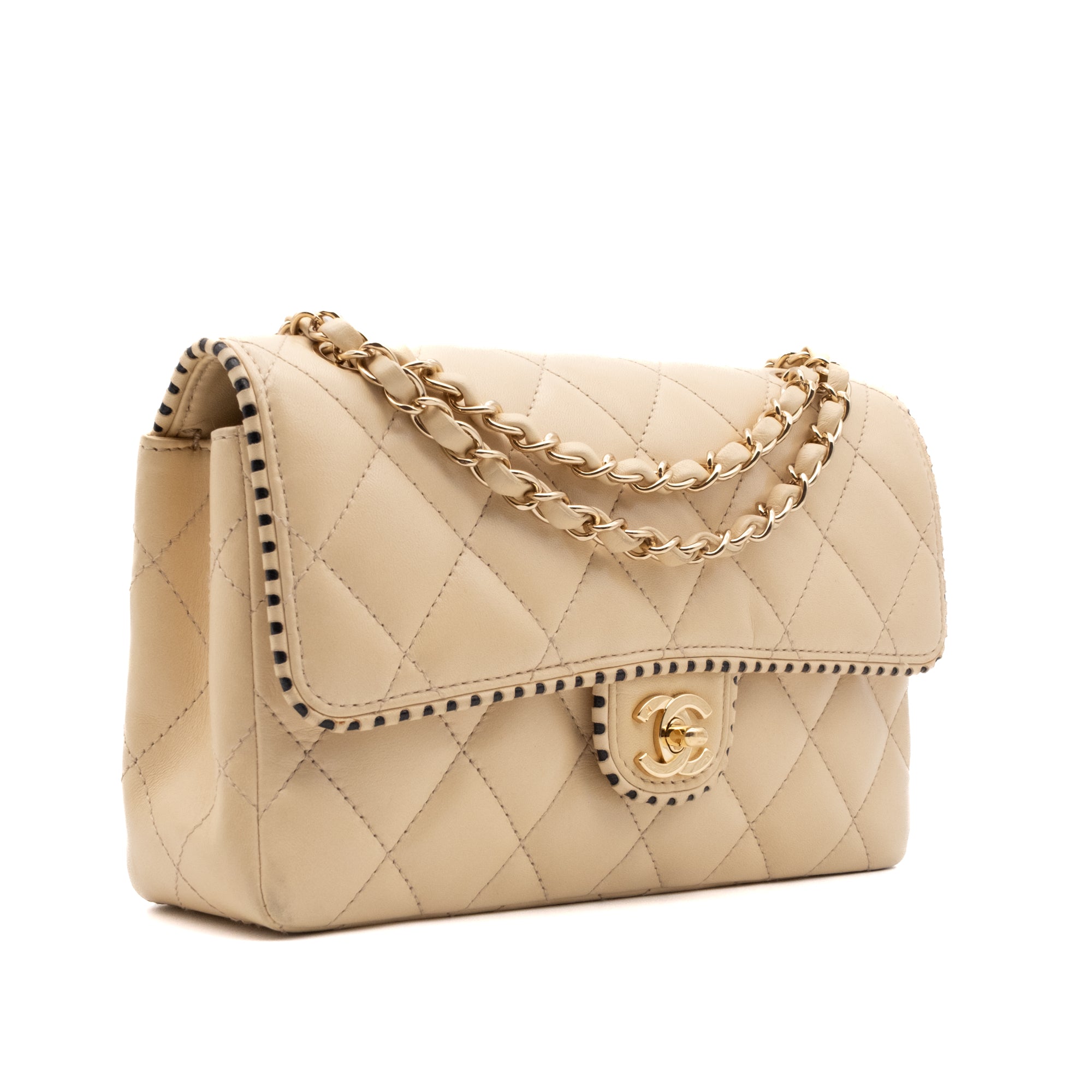 Beige Chanel Timeless Handtasche Single Flap Bag Medium Größe aus Lammleder Material mit goldener Hardware und schwarzer Trimm Zierborte halb Vorderseite links 